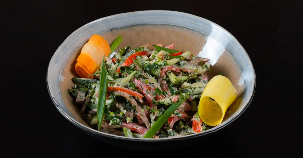Une salade de légumes vibrante avec une sauce crémeuse servie dans un bol en céramique sur un fond sombre.
