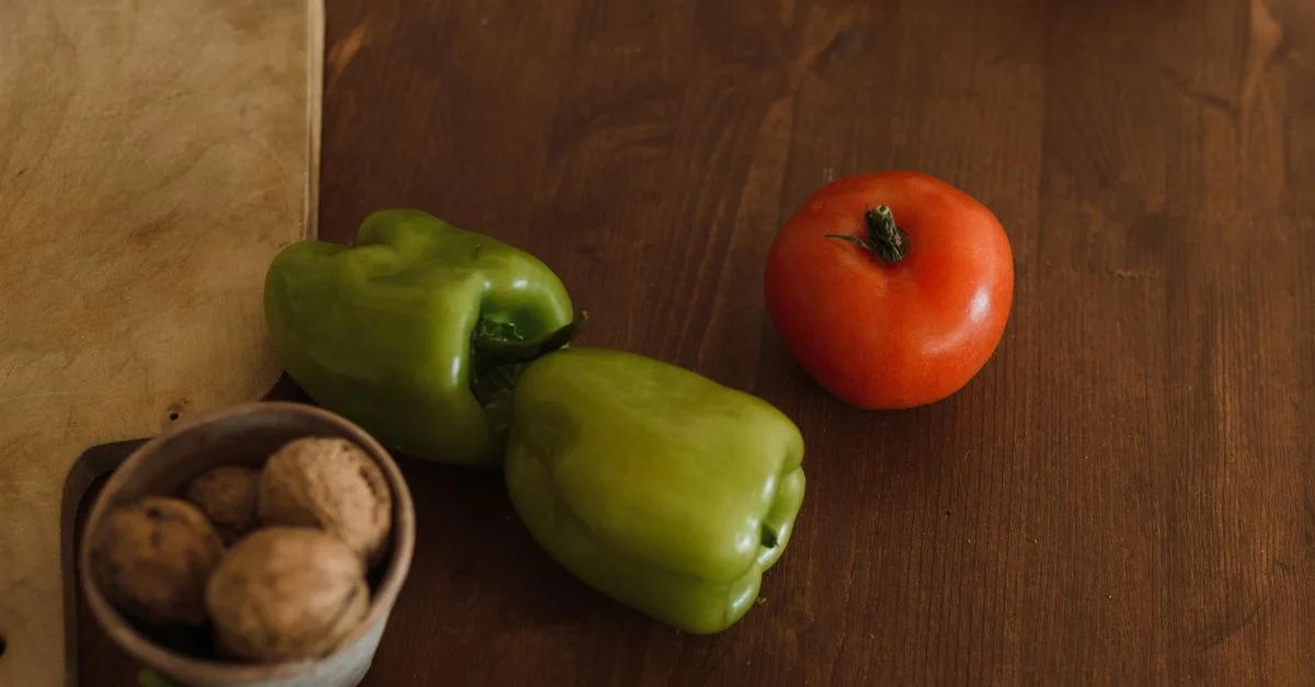 Un gros plan de poivrons verts frais et d'une tomate mûre sur une table en bois rustique, suggérant une alimentation saine.