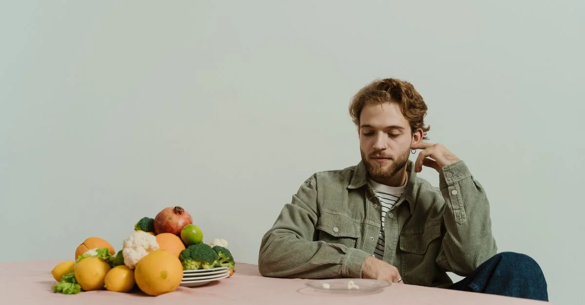 Un homme en tenue décontractée est assis à une table avec divers légumes, évoquant une humeur réfléchie.