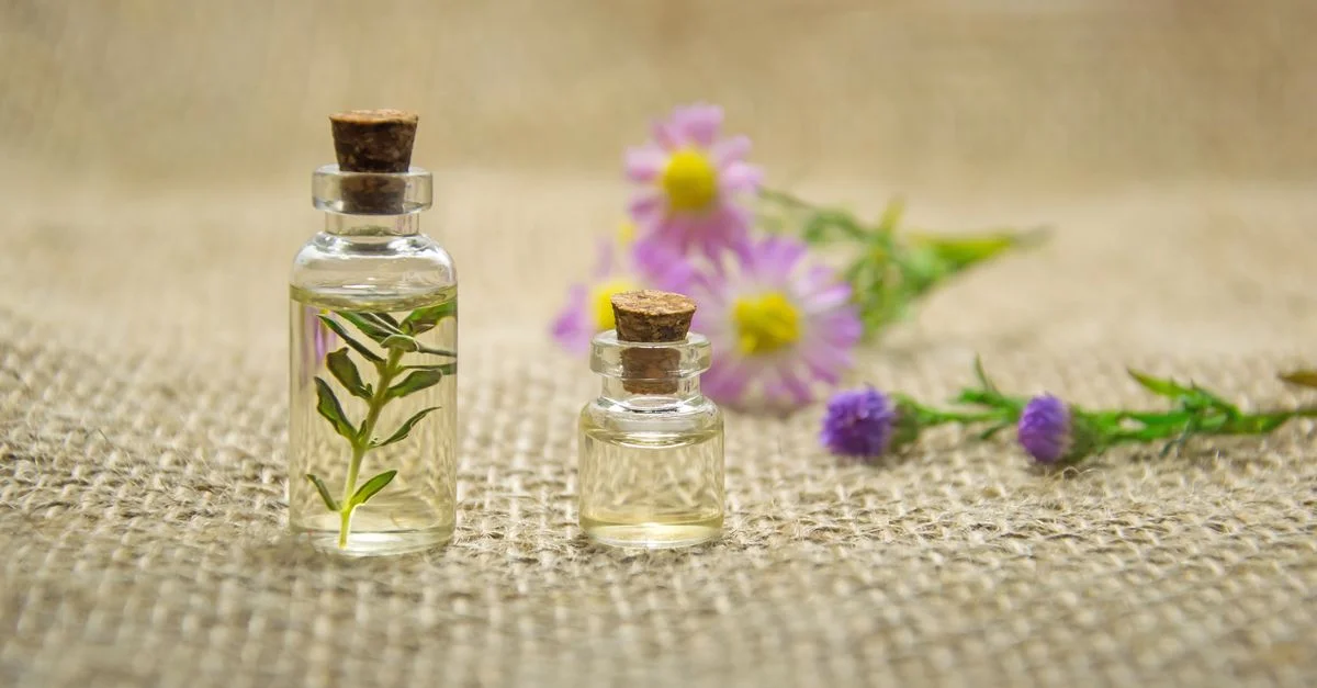 Bouteilles en verre avec des huiles essentielles et des fleurs fraîches sur un tissu en jute créant un arôme naturel.